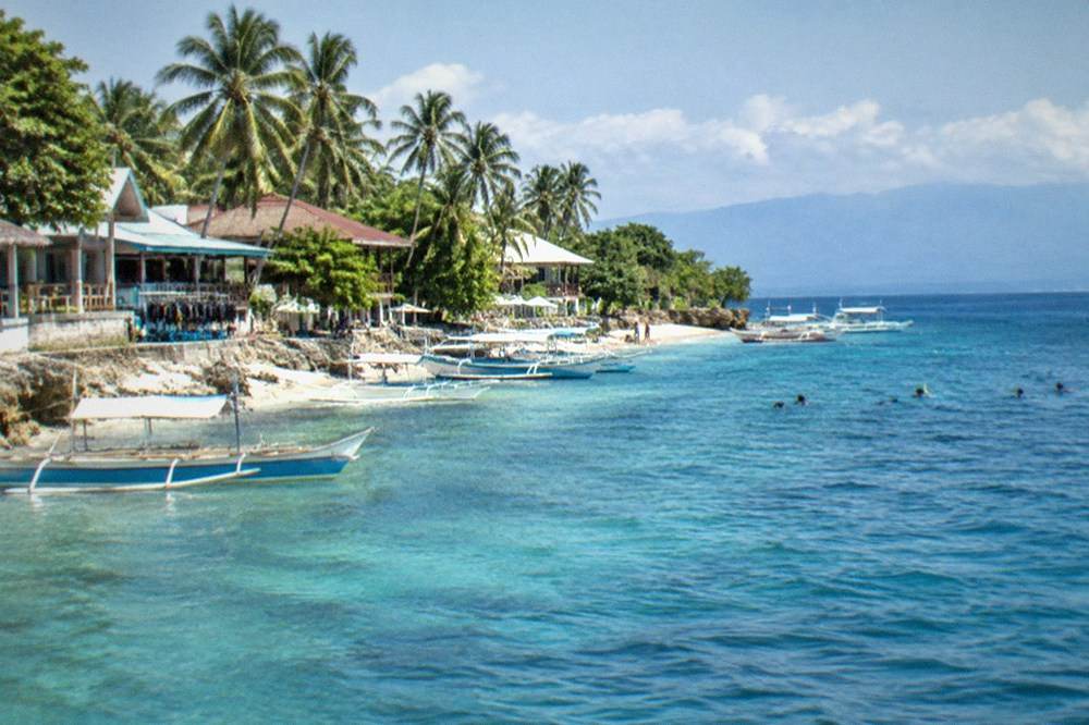 The waterfront of Panagsama Beach with dive shops and small outrigger boats along the shore