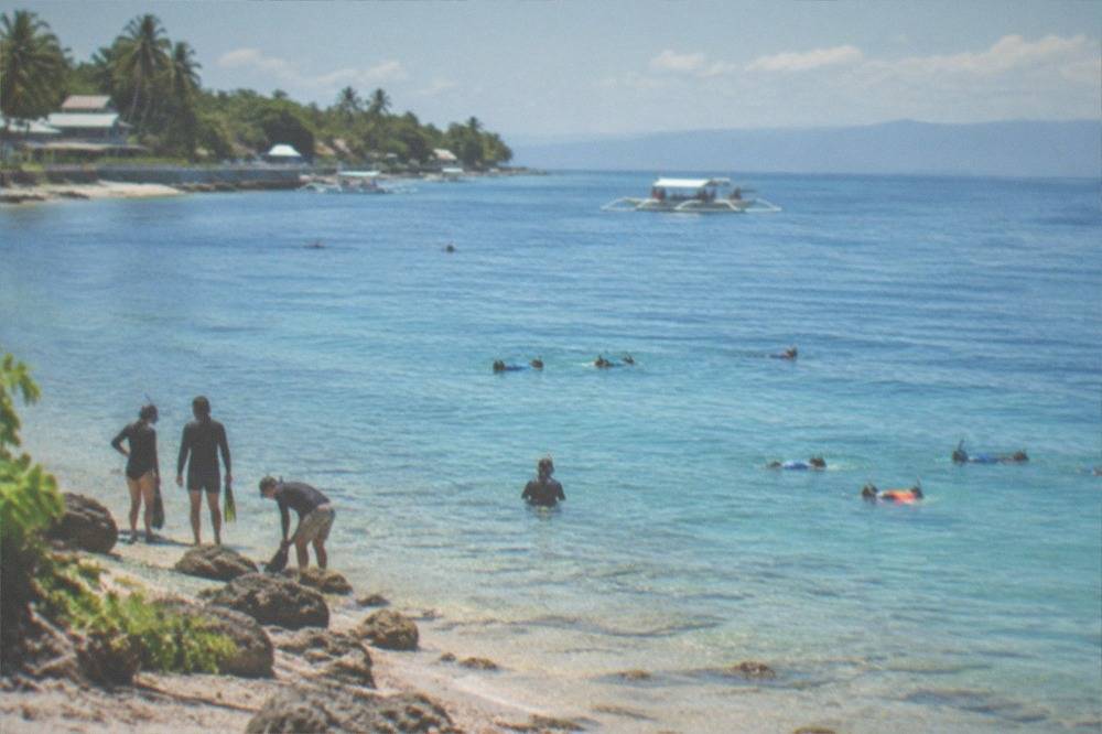 Early morning sunlight hitting calm water at a tropical beach with snorkelers preparing to enter