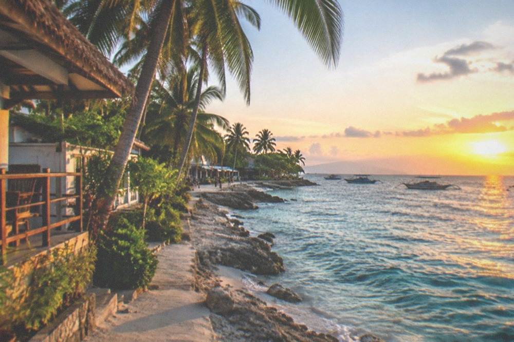 A guesthouse and palm trees along a beachfront lane in a Philippine coastal town at sunset