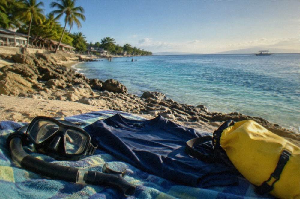 Snorkel gear, a rash guard and a dry bag laid out on a beach towel