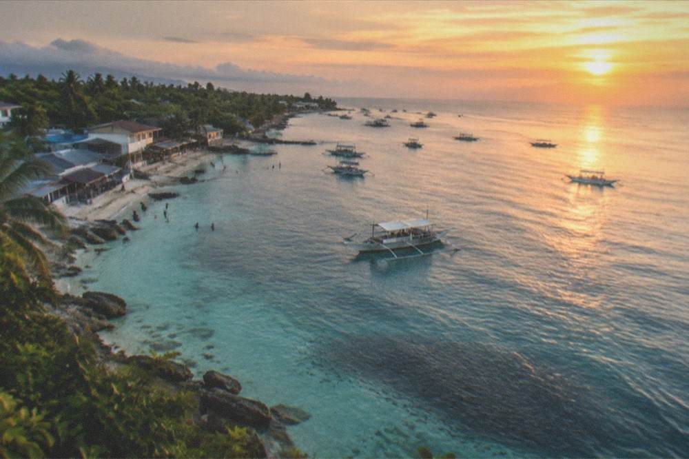 A wide view of a coastal town at golden hour with outrigger boats and calm sea