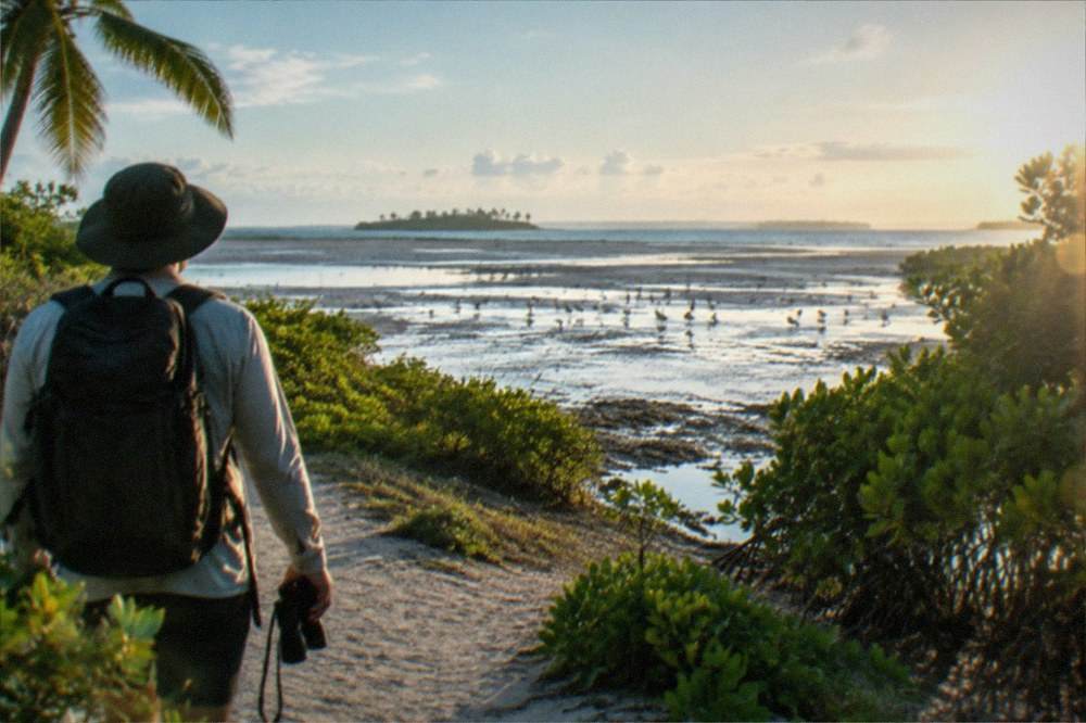 A visitor with binoculars and a hat walking a sandy trail toward the bird flats on Olango Island, Cebu, Philippines