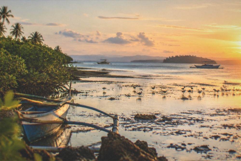 A quiet shoreline on Olango Island at golden hour with fishing boats and distant islands, Cebu, Philippines