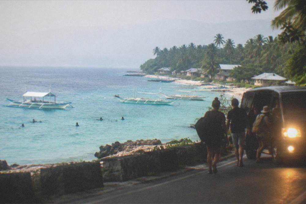 Travellers boarding a van in the dark with headlights illuminating a coastal road