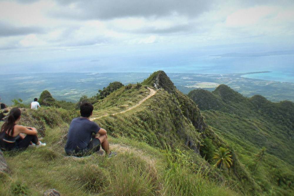 Hikers in casual clothes and sneakers resting on a grassy ridge with wide valley views