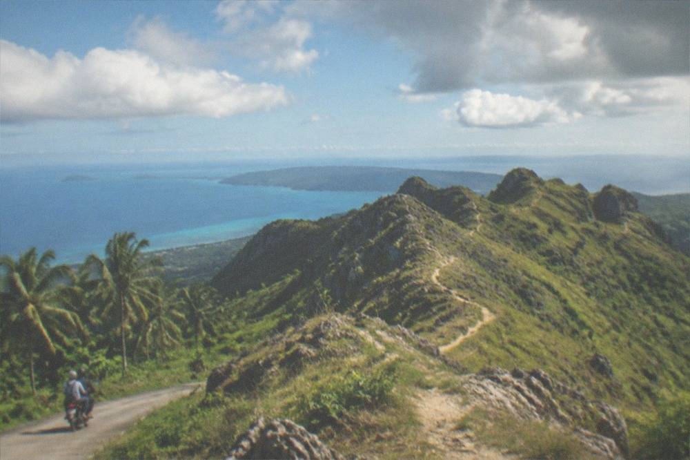 A motorbike taxi carrying two passengers along a rural road between coconut palms
