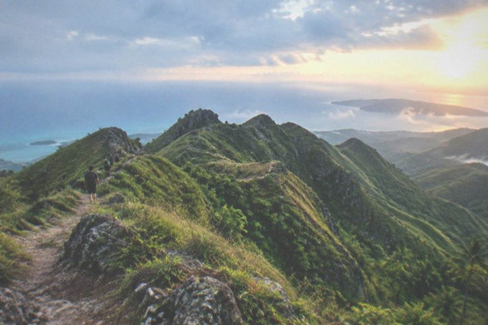Sunrise light spreading across folded green mountain ridges with thin mist in the valleys