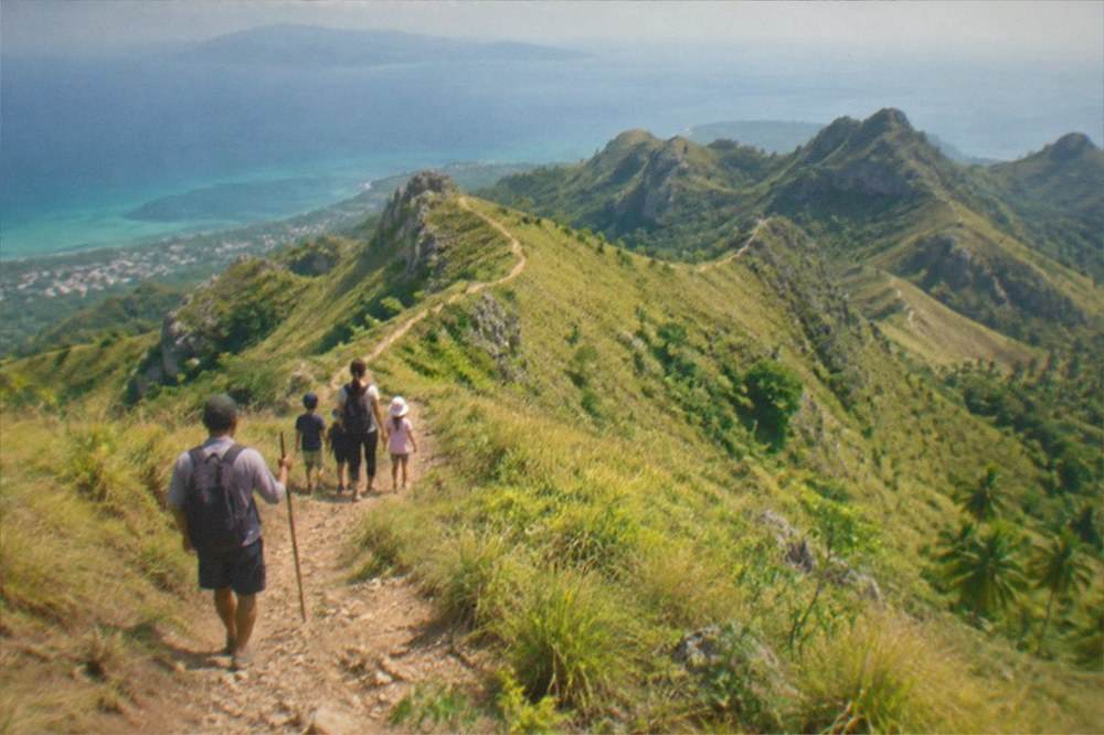 A family with children walking a grassy uphill path behind a local guide