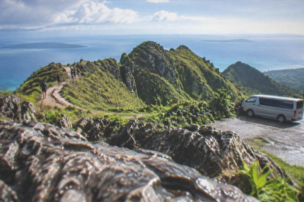 A tour van parked on a highland road with green ridges rising behind it
