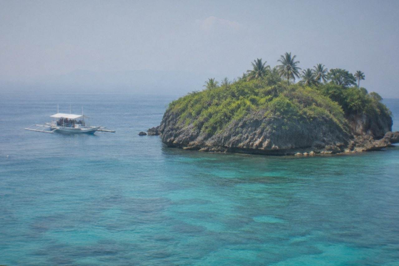 A small treeless island rising from calm blue sea, with a dive boat moored nearby