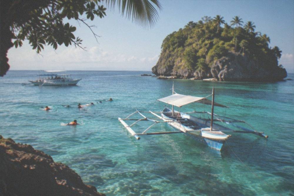A wooden outrigger boat anchored over turquoise water with snorkelers nearby