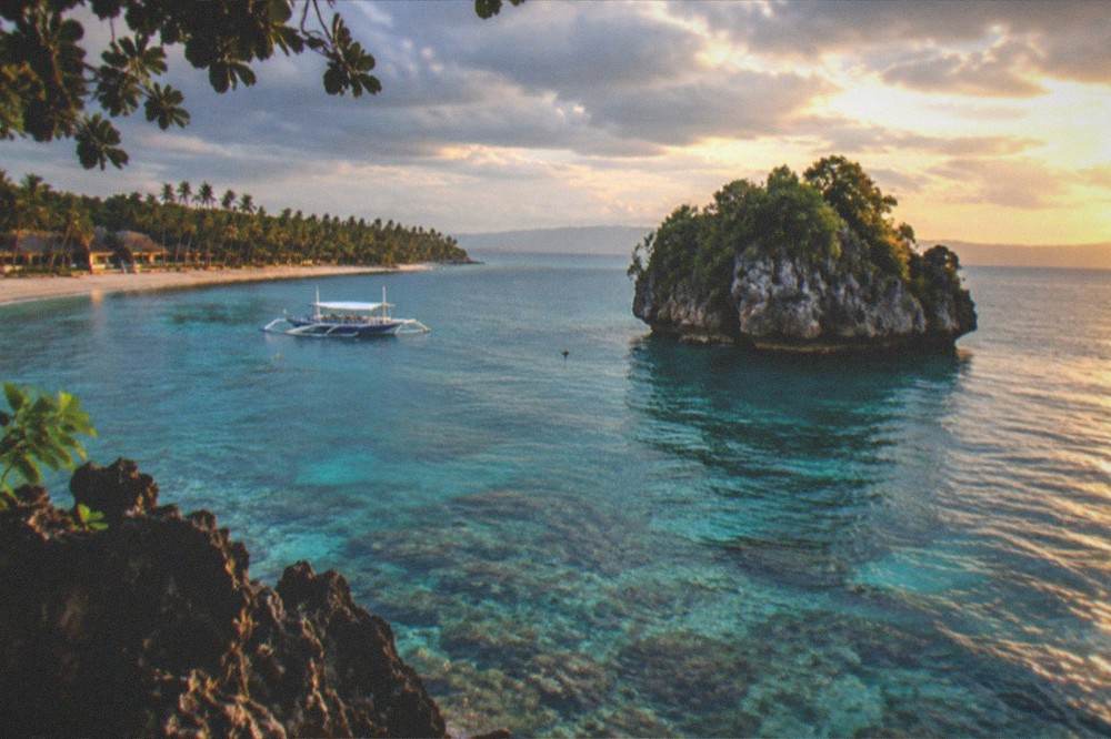 A beachfront row of small resorts and palm trees along a curved bay at golden hour