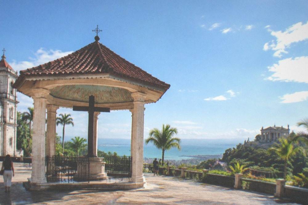 A stone temple with columns and statues on a hillside above Cebu City, seen under an afternoon sky