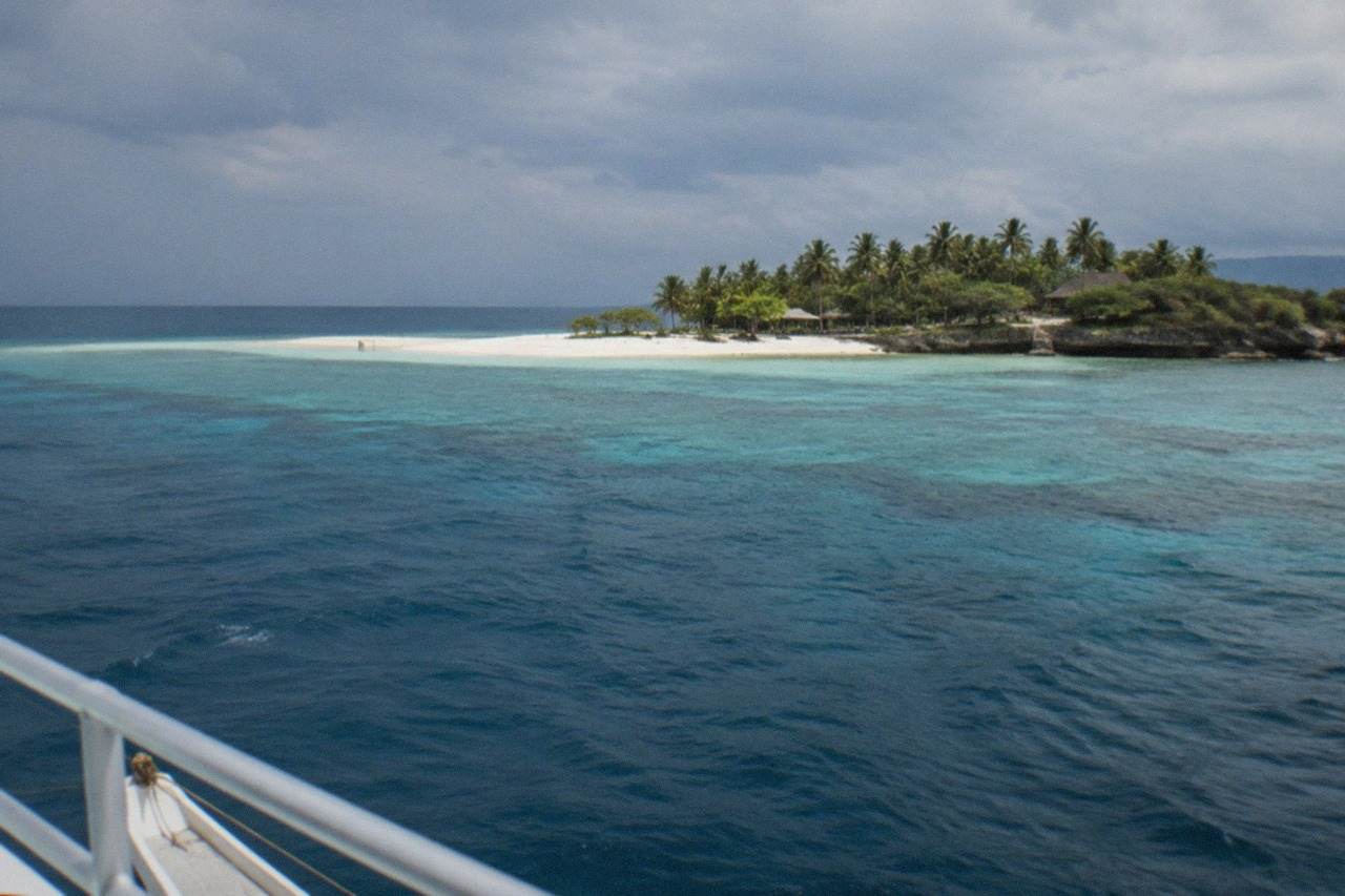 A small tropical island with a white sandbar and clear turquoise water seen from a boat