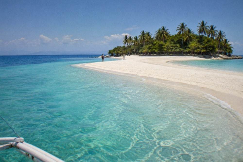 A wide white sandbar curving into shallow turquoise water under a blue sky
