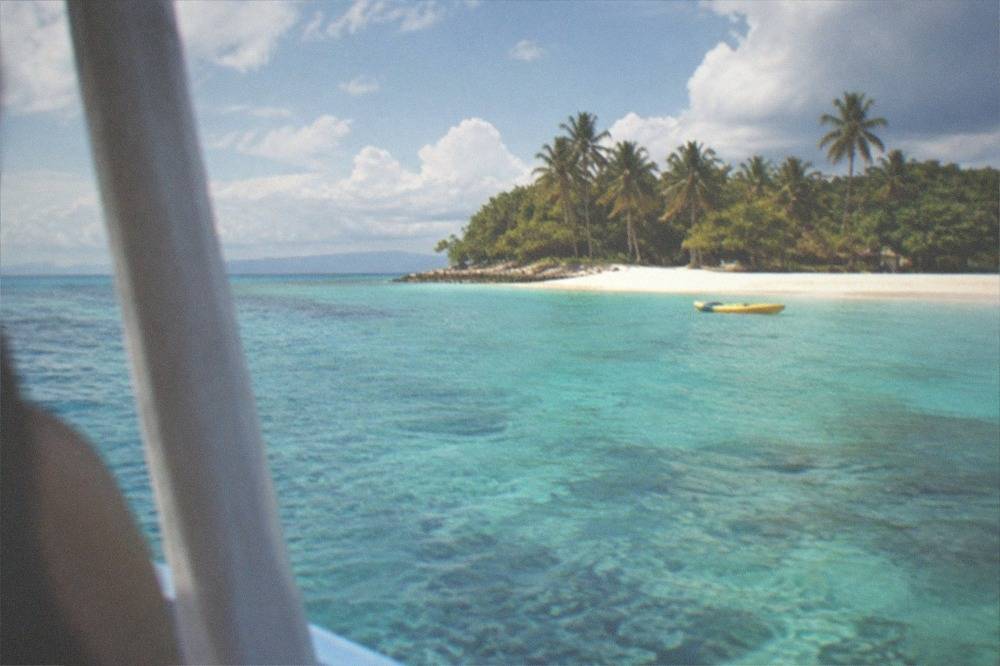 A turquoise lagoon inside a coral reef with a kayak floating near a sandy beach