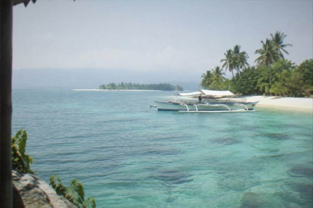 A wooden outrigger boat anchored beside a white sand beach with coconut trees