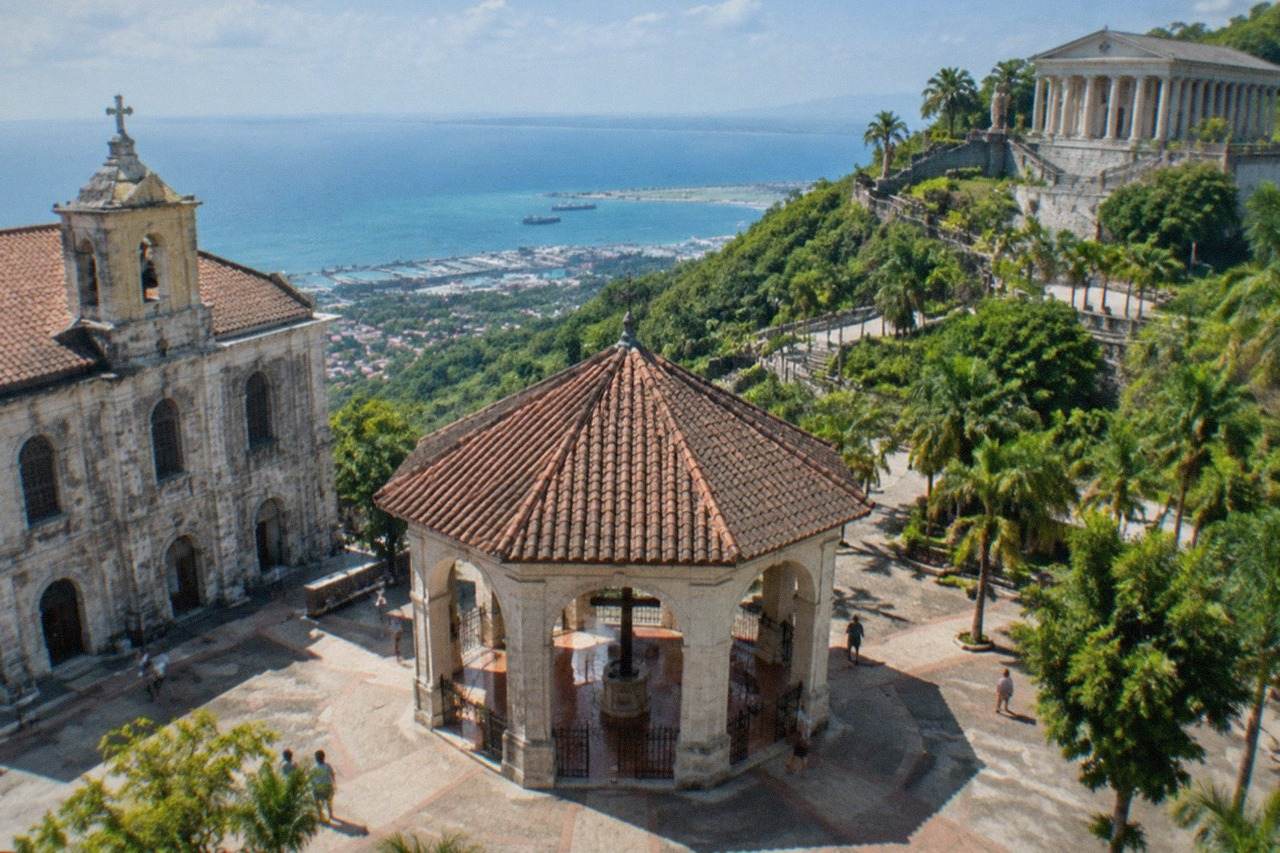 A large stone temple with tall columns and statues standing on a green hillside above Cebu City