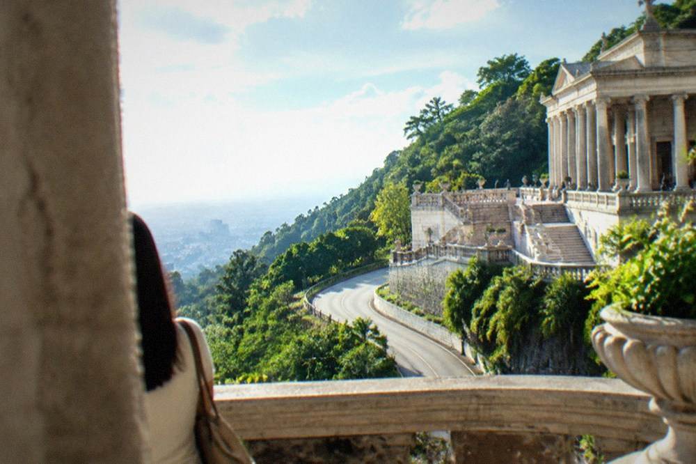 A paved winding mountain road climbing through green hills toward a hilltop temple