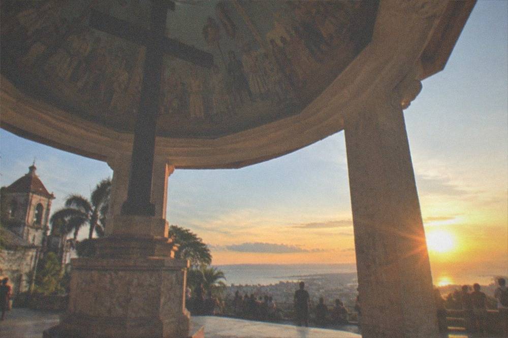 Crowd of visitors on a hilltop deck watching an orange sunset over a coastal city and sea