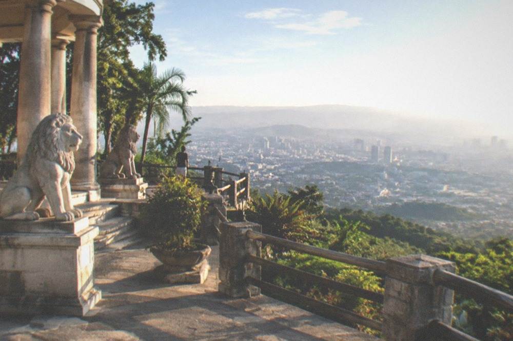 Stone mansion shrine with columns and lion statues on a tropical hillside