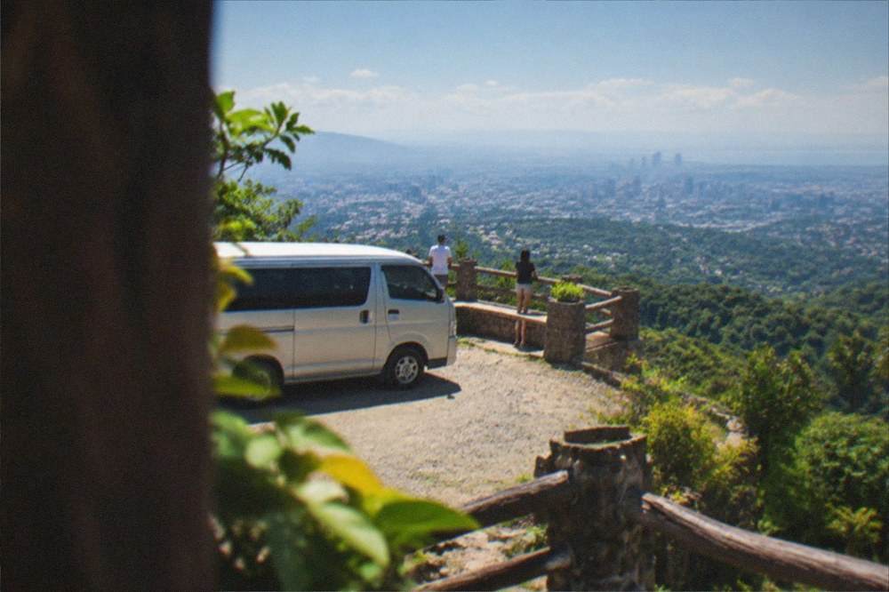 Small tour van parked at a hilltop viewpoint with tropical hills behind it