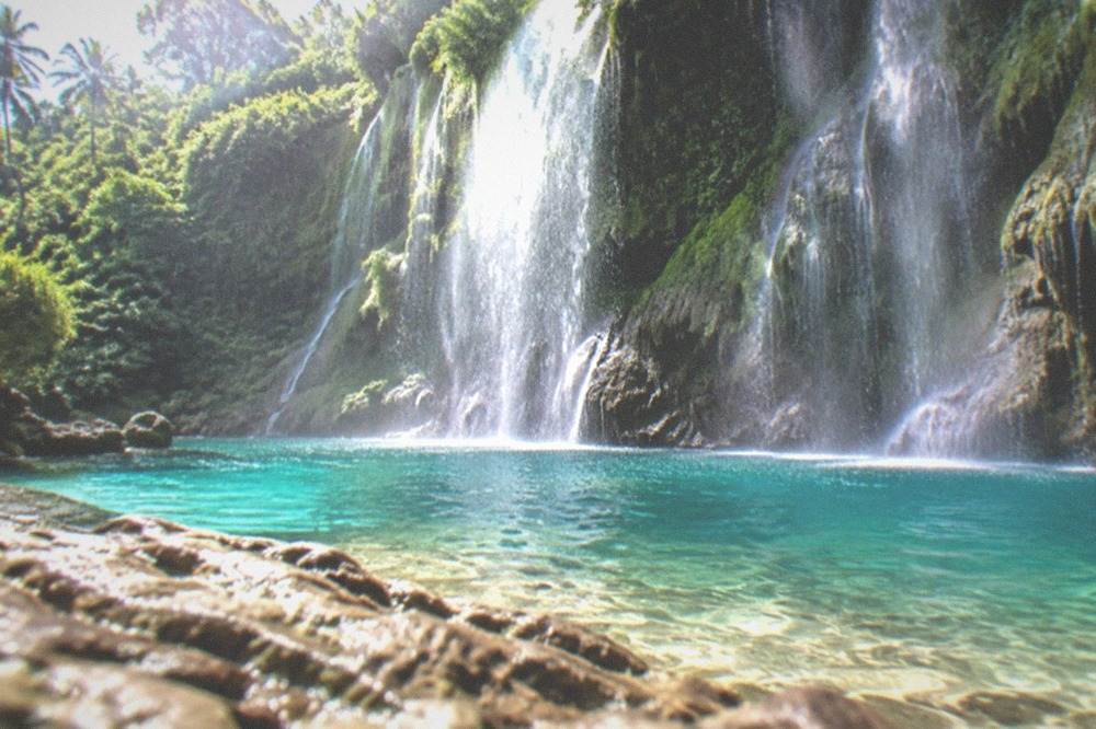 Morning sunlight reaching a green waterfall cliff while the pool below is still empty