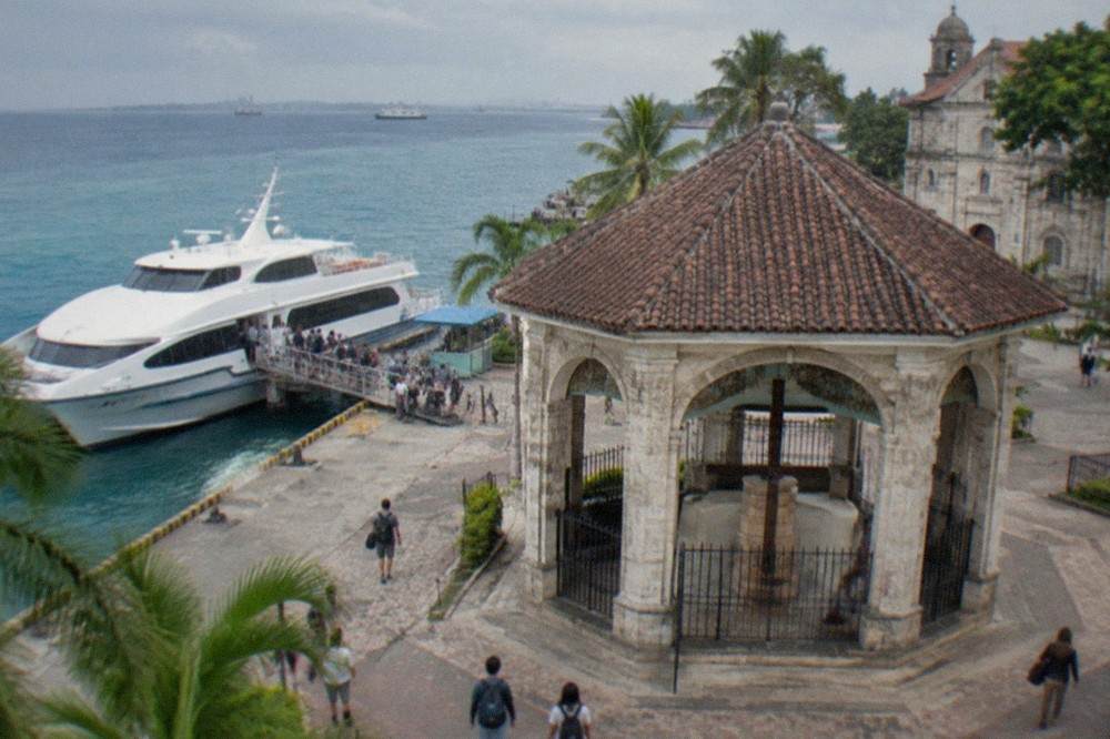 Passengers boarding a white fastcraft ferry at a busy pier in Cebu City in the early morning