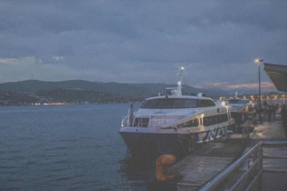 A ferry terminal at dusk with a fastcraft moored at the pier and city lights along the waterfront