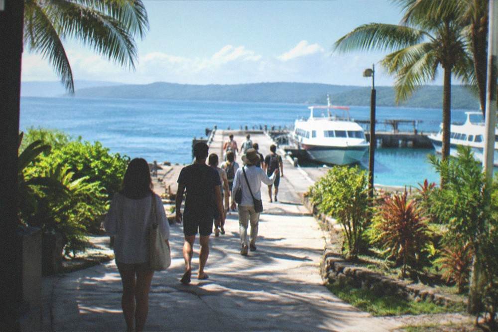 Travellers in light clothing walking with a guide along a paved path between tropical plants in Bohol
