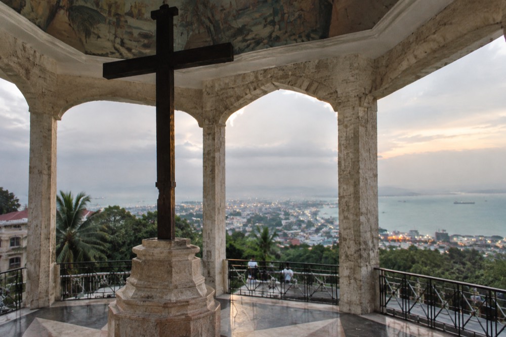 A viewing deck above a city at dusk with lights spreading along a coastline below