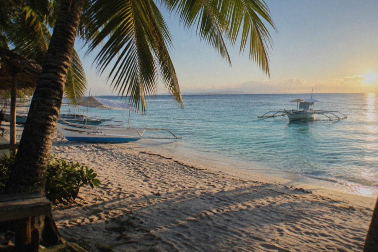 A small outrigger boat moored in clear shallow water off a tropical island beach at sunrise