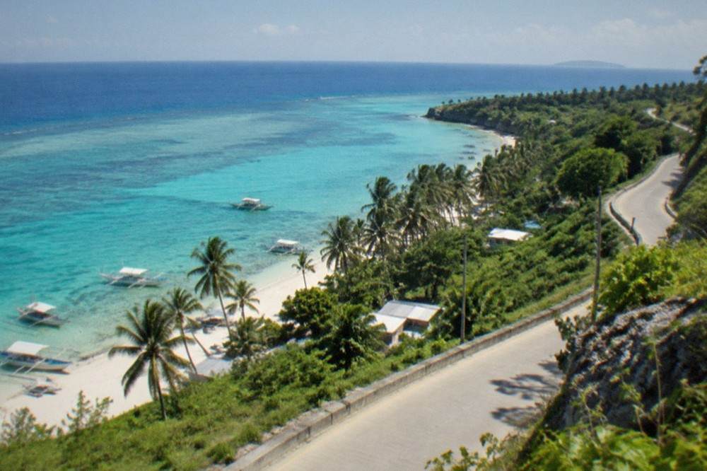 A coastal road winding past green hills with the sea visible in the distance