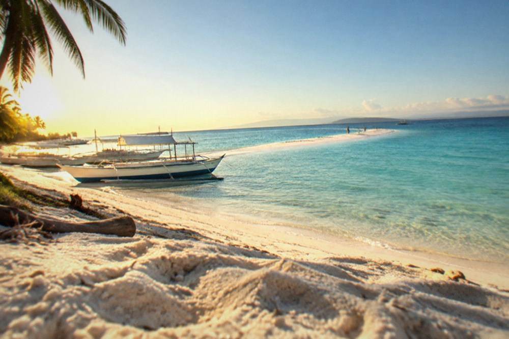 A long white sand spit stretching into calm turquoise water under a blue sky