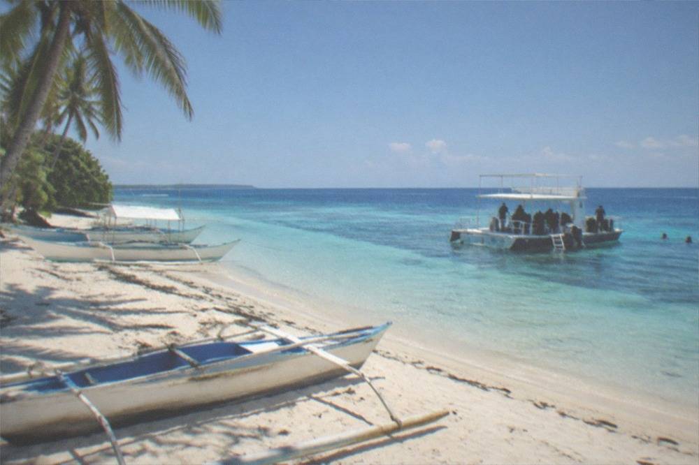 A dive boat anchored over a shallow reef with divers preparing gear on deck