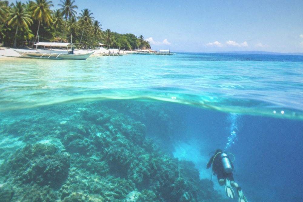 A diver descending through blue water toward a submerged reef shelf