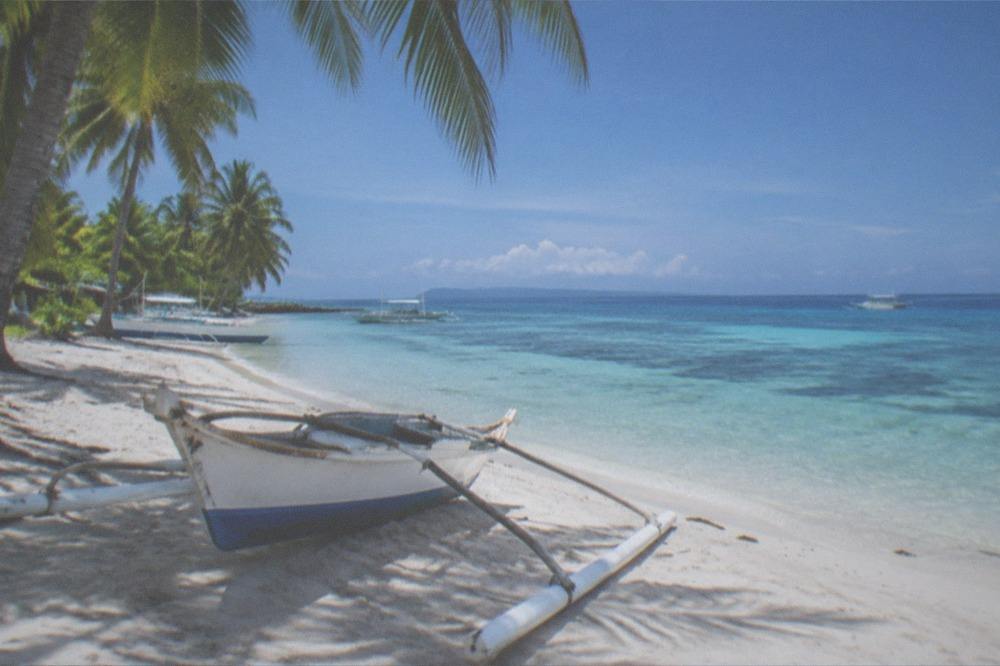 A palm-fringed white sand beach with a wooden outrigger boat pulled up on the sand