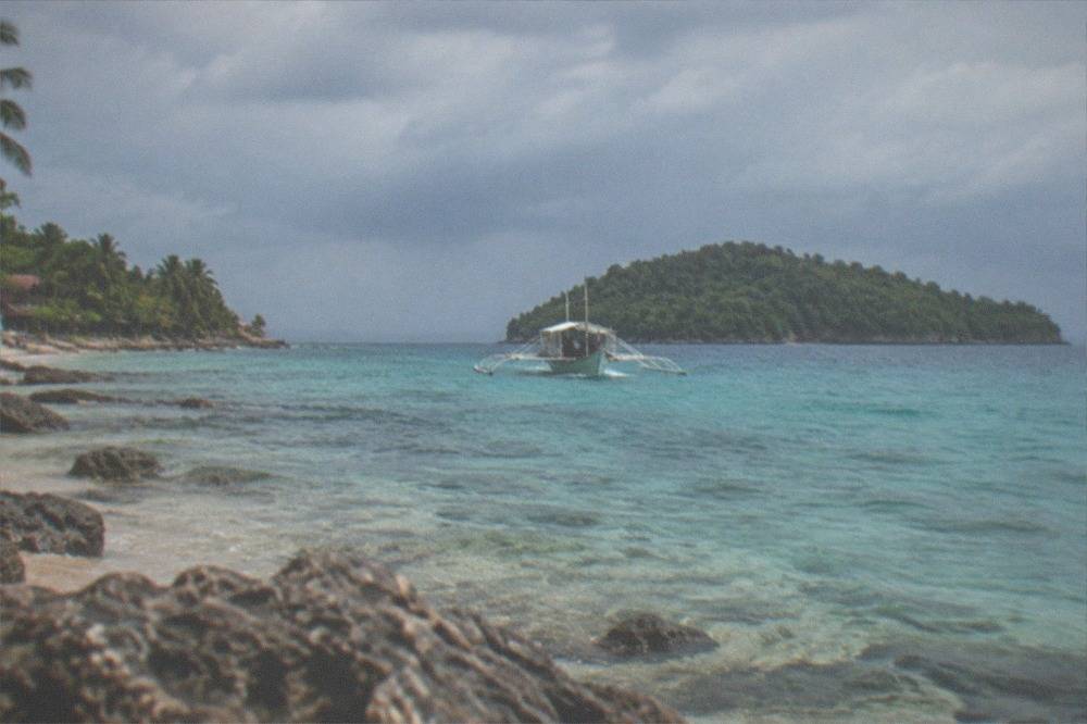 A small outrigger boat approaching a green island with clear turquoise water