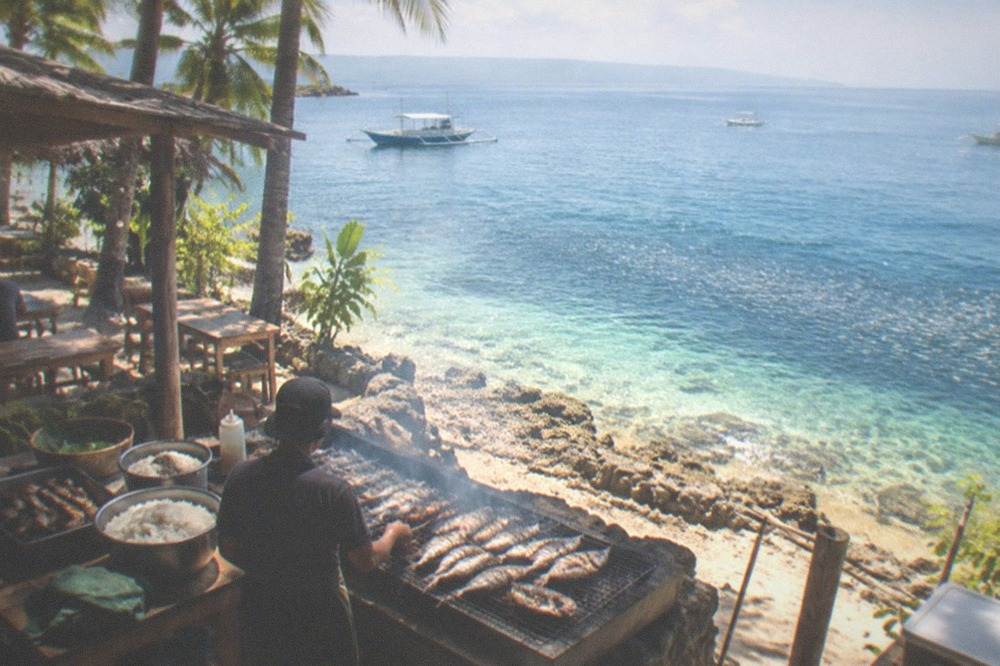 A beachside grill preparing fresh fish and rice at a small open-air restaurant