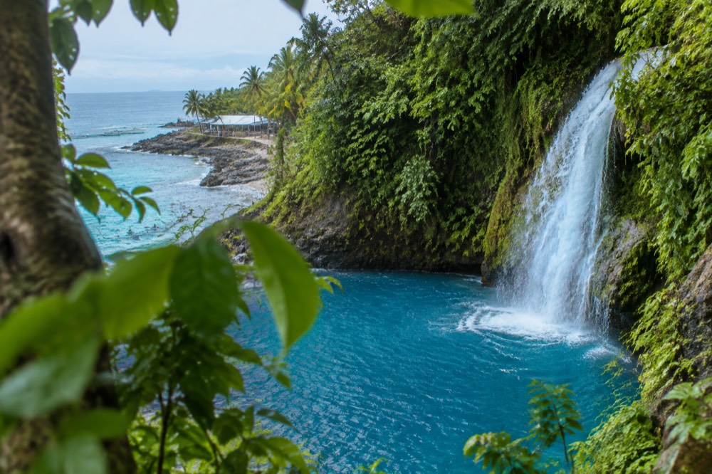 A turquoise waterfall plunging into a deep blue pool surrounded by jungle