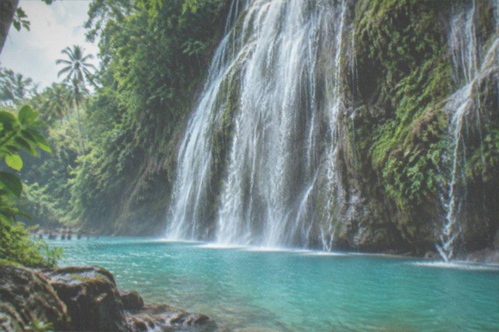 Cold turquoise water pouring over the wide rock face of Tumalog Falls