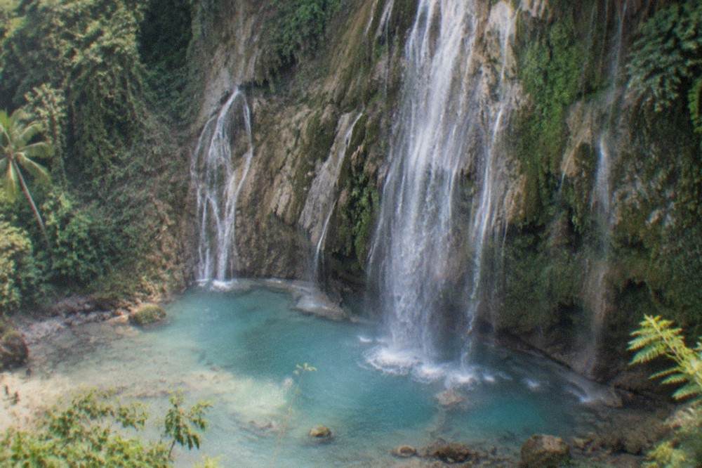 Turquoise water pouring over the wide rock face of Tumalog Falls near Oslob