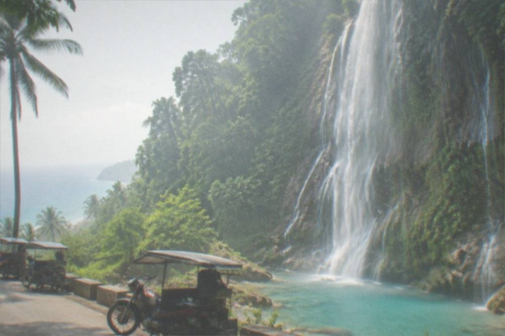 Motorcycle taxis parked on a coastal road above the blue pool of Tumalog Falls