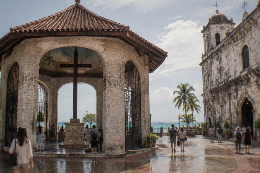 Tourists walking among colonial-era stone buildings in Cebu City on a bright dry-season day