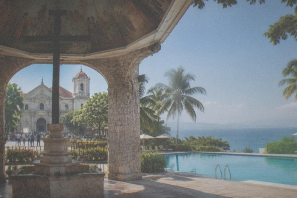A calm resort swimming pool with palm trees under a clear morning sky in Cebu