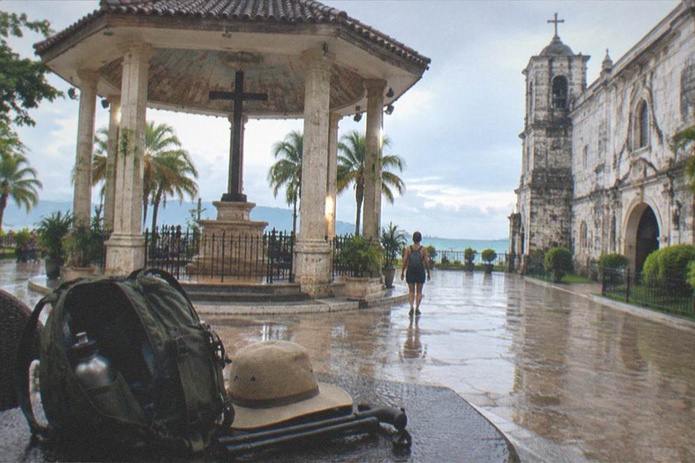 A traveler's open daypack with a water bottle, sun hat and folded walking cane on a resort table
