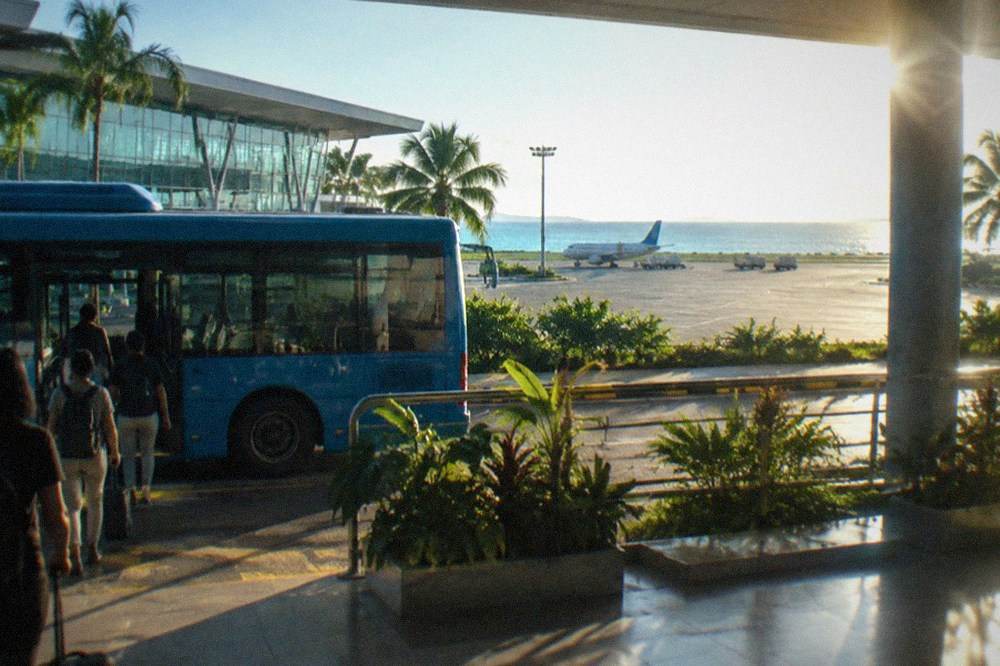 A blue air-conditioned bus parked at an airport curb with passengers boarding