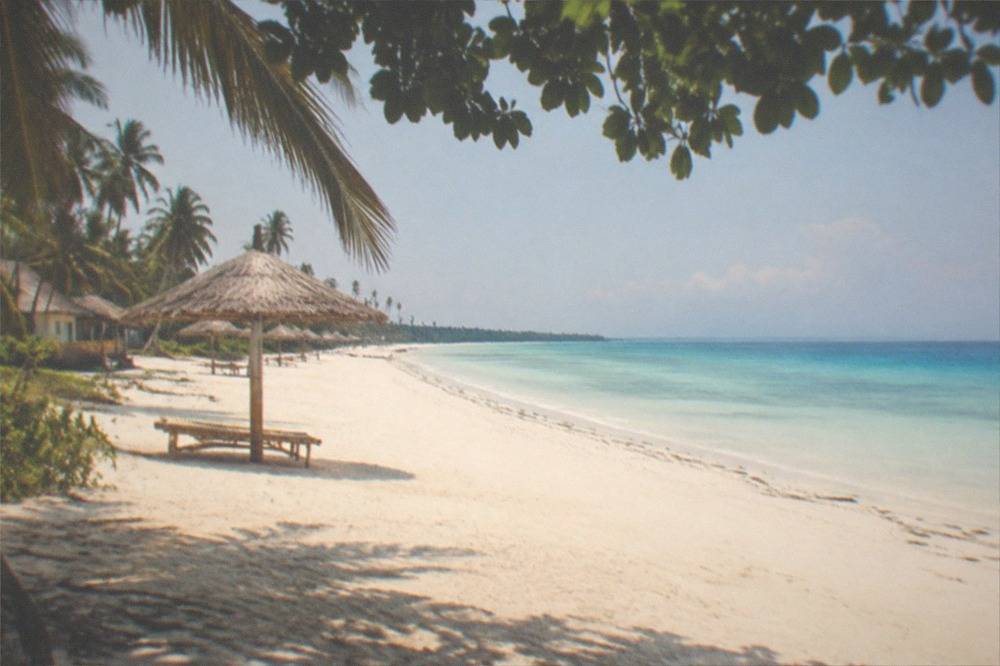 A long empty white sand beach with a few bamboo umbrellas on Bantayan Island, Cebu