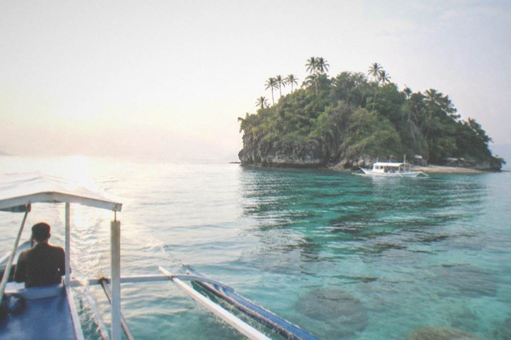 A dive boat crossing calm turquoise water toward an island at sunrise