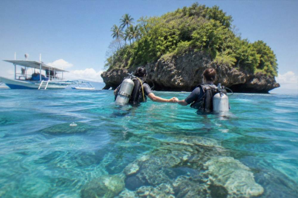 An instructor guiding a new diver over a shallow reef holding hands